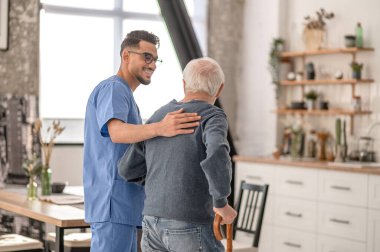 Nurse helping his patient to walk with a walking stick clipart