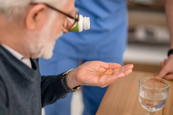 Gamle man som får läkemedel från en sjuksköterska i hemmet — Stockfoto