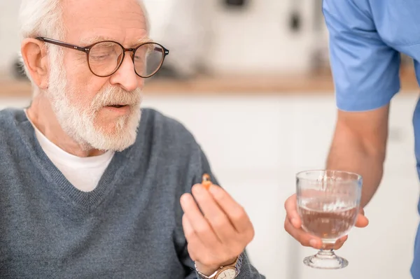 Pensionista tomando una pastilla con agua supervisada por su cuidador — Foto de Stock