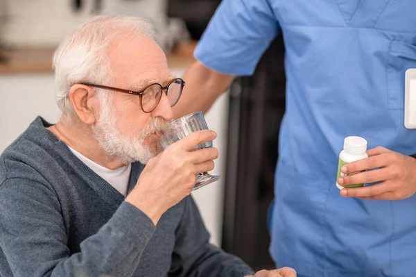 Starší muž užívající léky pod dohledem zdravotnického pracovníka — Stock fotografie