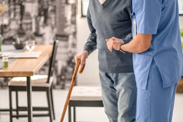 Trabajador médico ayudando a su paciente a caminar con un bastón — Foto de Stock
