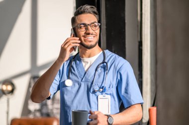 Gözlüklü yakışıklı doktor cep telefonuyla konuşuyor.