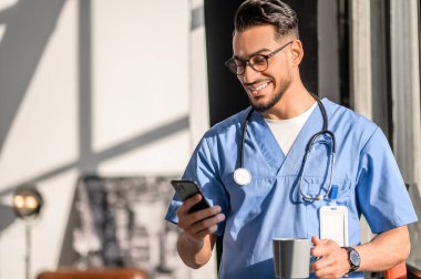 Çay molasında gözlüklü doktor cep telefonunu kullanıyor.