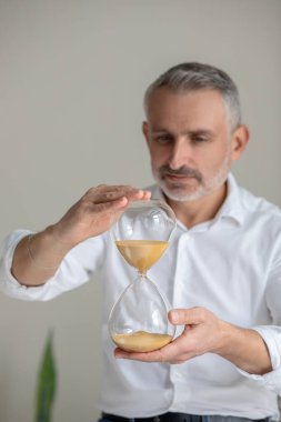 Elinde kum saati olan beyaz gömlekli bir adam.