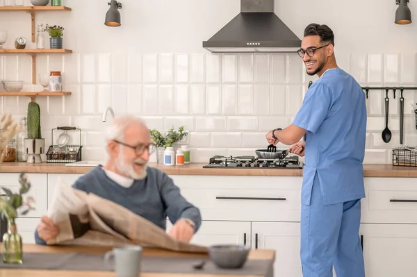Cheerful caretaker preparing breakfast for an aged man — Foto de Stock