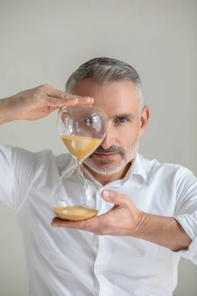 Um homem de camisa branca com um relógio de areia nas mãos — Fotografia de Stock