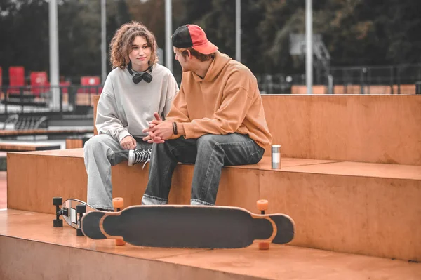 Guy and girl with skateboards talking sitting in park — стоковое фото