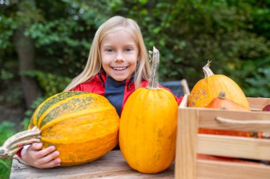 A cute girl standing near the table with pumpkins on