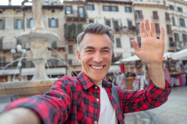 Man smiling at camera raising hand in greeting