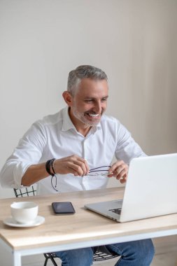 Gözlüklü neşeli adam dizüstü bilgisayara bakıyor.