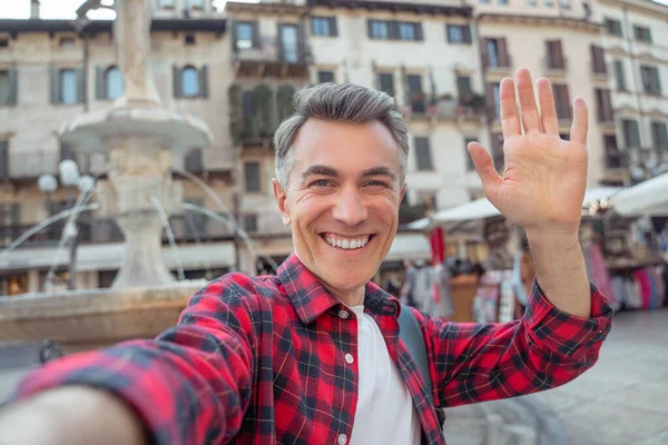 Man smiling at camera raising hand in greeting — Stockfoto