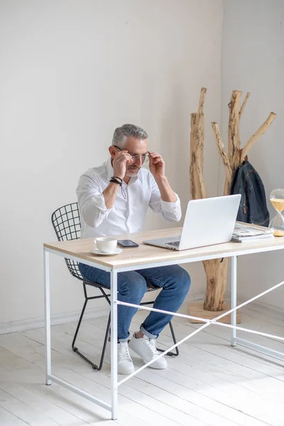 Man putting on glasses sitting at table with laptop — Fotografia de Stock