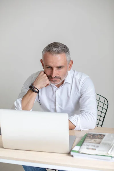 Przemyślany mężczyzna patrzący na laptopa dotykający twarzy pięścią — Zdjęcie stockowe