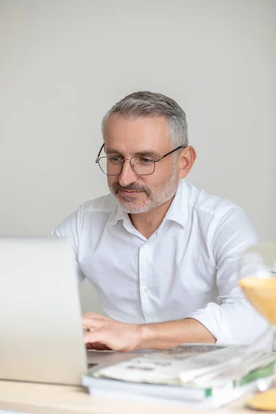 Мужчина в белой рубашке и очках работает в офисе и выглядит вовлеченным — стоковое фото