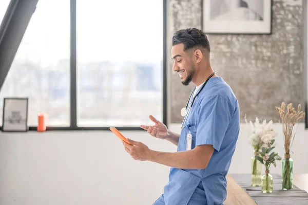 Pleased healthcare worker using his gadget indoors — Fotografia de Stock