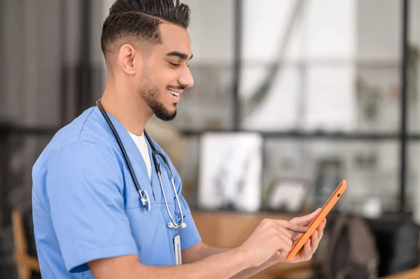 Fokuserad glad läkare skriva på sin gadget — Stockfoto