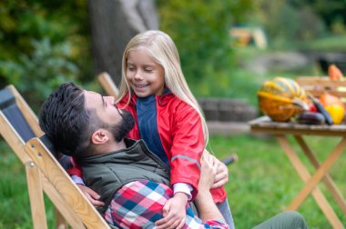 Koyu saçlı bir adam ve kızı çiftlikte vakit geçiriyorlar.