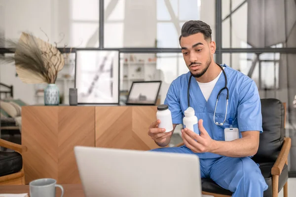 Doctor con frascos de pastillas en sus manos en el portátil —  Fotos de Stock