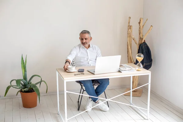 Homem sentado à mesa com laptop tocando copo — Fotografia de Stock