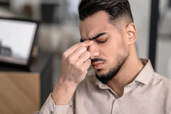 Un hombre moreno tocándose el puente nasal y con dolor de cabeza — Foto de Stock