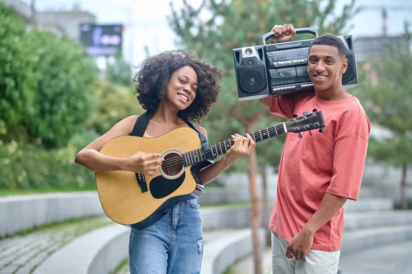 Meisje met gitaar jongen met platenspeler kijkend naar camera — Stockfoto