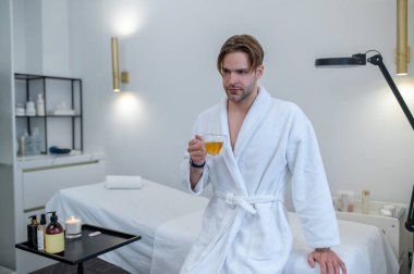 Çay zamanı. Elinde çay tutan beyaz cüppeli genç adam.