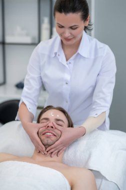 Yüz masajı. Kaplıca salonunda yüz masajı yaptıran genç bir adam.