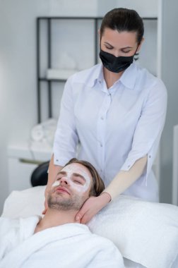 Boyun masajı. Yüzünde maske olan genç bir adam boyun masajı yaptırıyor.
