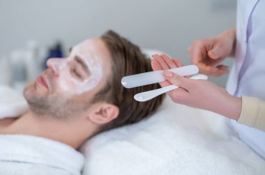 Güzellik salonunda. Güzellik salonunda yüz maskesi takmış bir adamı yakından çek.