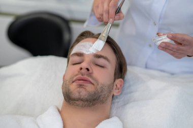 Yüz maskesi. Kozmetik uzmanı müşterilerin yüzüne fırçayla krem sürüyor.