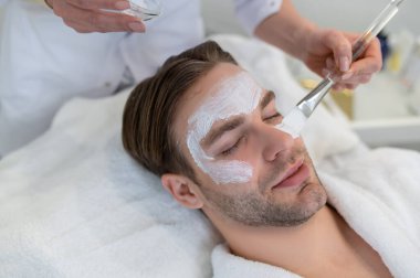 Yüz bakımı. Yüzünde nemlendirici maske olan bir adama yaklaş.