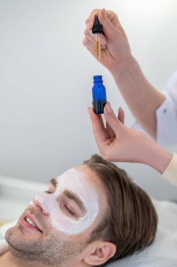 Yaş karşıtı serum. Güzellik uzmanı erkek yarık yüzüne serum uyguluyor.