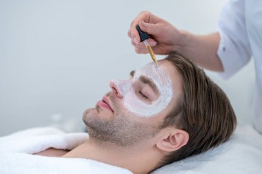 Yaş karşıtı serum. Güzellik uzmanı erkek yarık yüzüne serum uyguluyor.