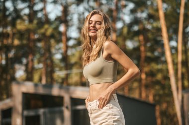 Gülümseyen güzel, şık, beyaz bir kadın yazlığına karşı kameraya poz veriyor.