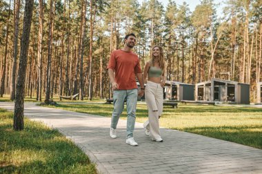 Gülümseyen güzel sarışın kadın ve onun yakışıklı erkek arkadaşı el ele yürüyorlar.