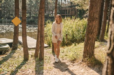 Gülümseyen şık, güzel, sarışın, beyaz bir kadın ahşap iskeleden uzaklaşıyor.