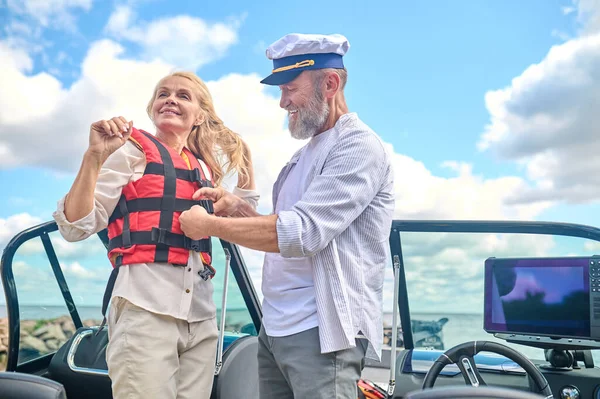 Life vest. A man in helping a blonde woman to put on the life vest