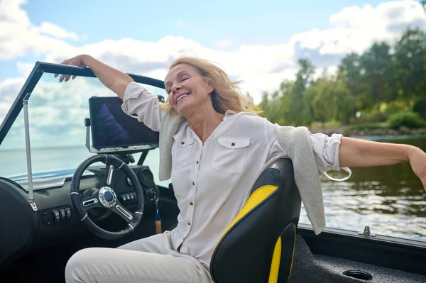 Relaxed. Blonde woman sitting in a boat and looking relaxed