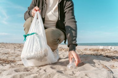 Çevreci bir aktivistin, kumdan atılmış plastik bir şişeyi alırken çekilmiş bir fotoğrafı.