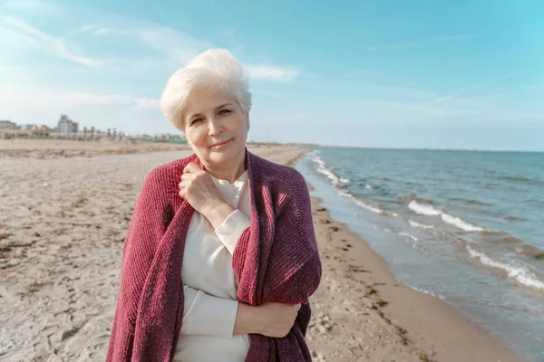 一位迷人的老年妇女独自站在海滩上向前看 — 图库照片