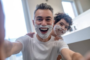 Komik tıraş. Baba ve oğul, yüzlerinde tıraş köpüğüyle tuhaf görünüyorlar.