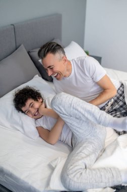 Sabah eğlencesi. Baba ve oğul sabah yatakta eğleniyor ve neşeli görünüyorlar.