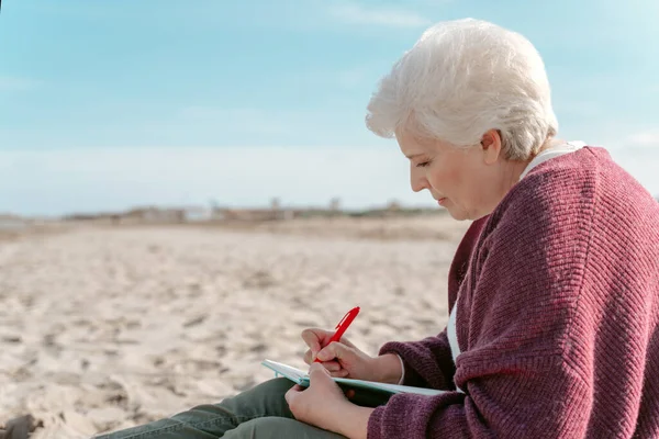 砂の上に座って日記を書いている女性作家の側面図 — ストック写真