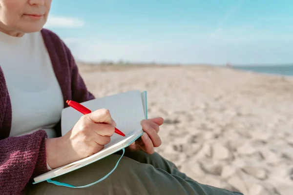 ノートにメモをとって海のそばのビーチに座っている医者の作物の写真 — ストック写真