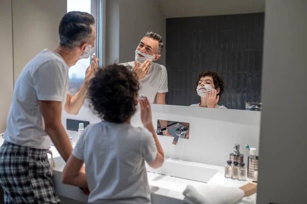 Shaving. Dad and son having mens morning procedures in the bathroom