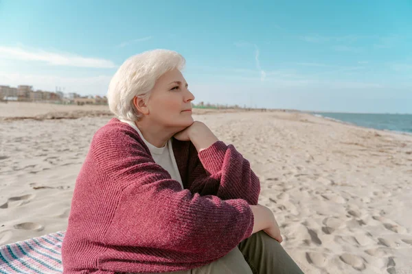 海のそばの砂の上に座って遠くを見る穏やかな女性 — ストック写真