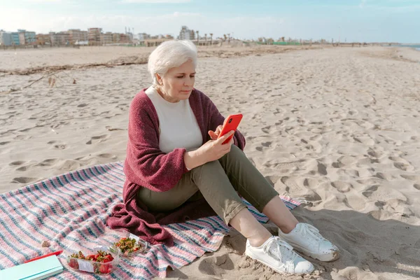 真剣に焦点を当てた女性座っている砂と彼女の手でスマートフォンを見て — ストック写真