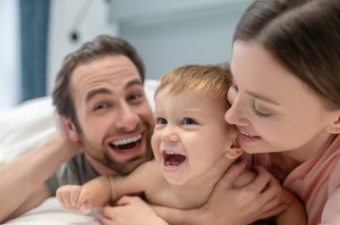 Neşeli olmak. Sevimli bir çocuk kadın ve ağzı açık yatağında uzanmış kameraya bakan bir adamın neşeli yüzleri.