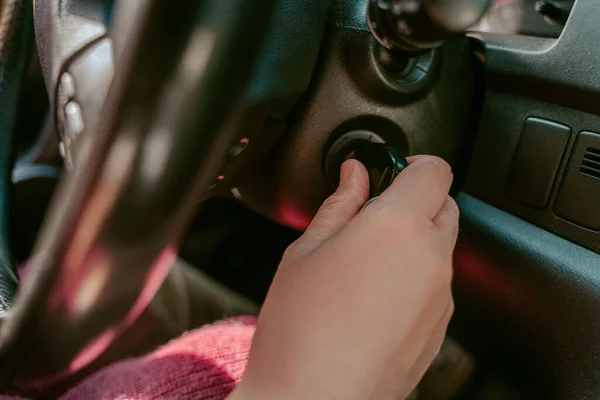 Closeup of a chauffeur seated at the car steering wheel turning the key in the ignition switch