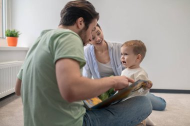 Birlikte oynuyoruz. Genç ebeveynler oğluyla oynuyorlar ve ona bir şey gösteriyorlar.